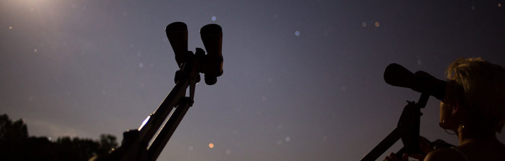 A woman looking through an astronomical binocular outdoors