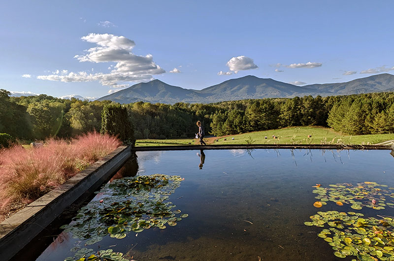 A reflecting pool with mountains in the background and a small child walking behind the reflecting pool