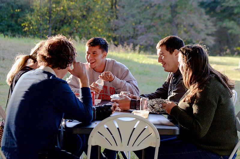 Five people sitting at a table outdoors, eating